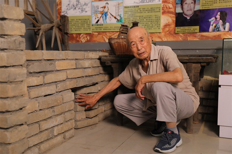 1755127040212870.jpg 图3:7月2日,李智凛在李家小院,演示土炕下的地道口模型。.jpg